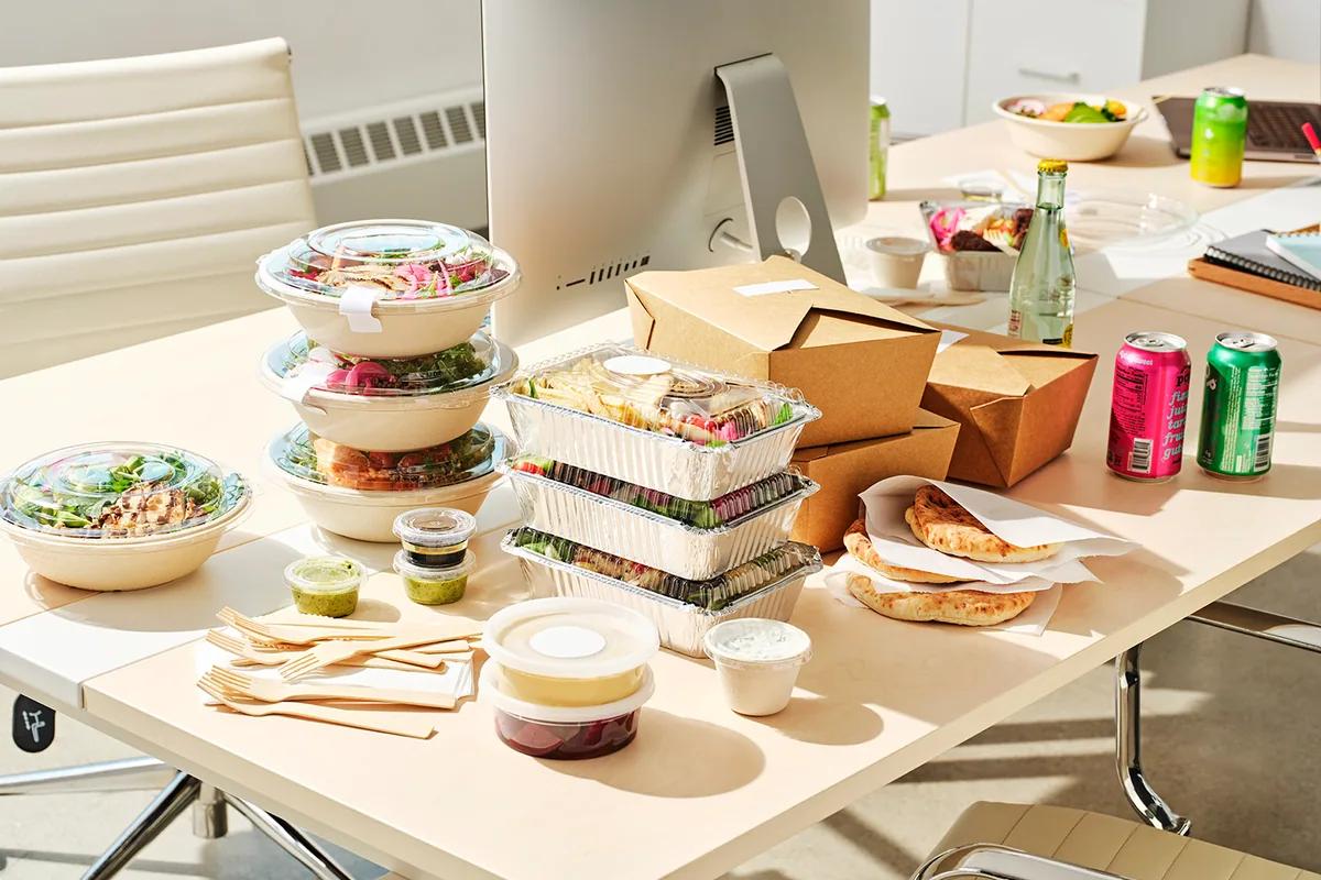 Packed lunches stacked on an office desk beside a monitor