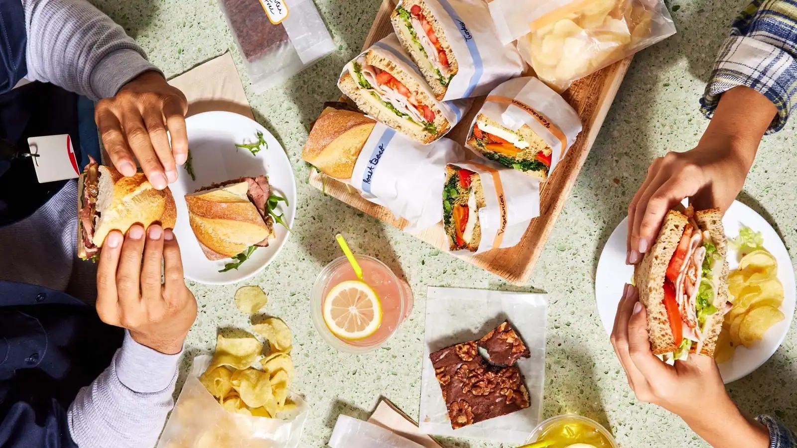 Colleagues holding wrapped sandwiches at a shared lunch table