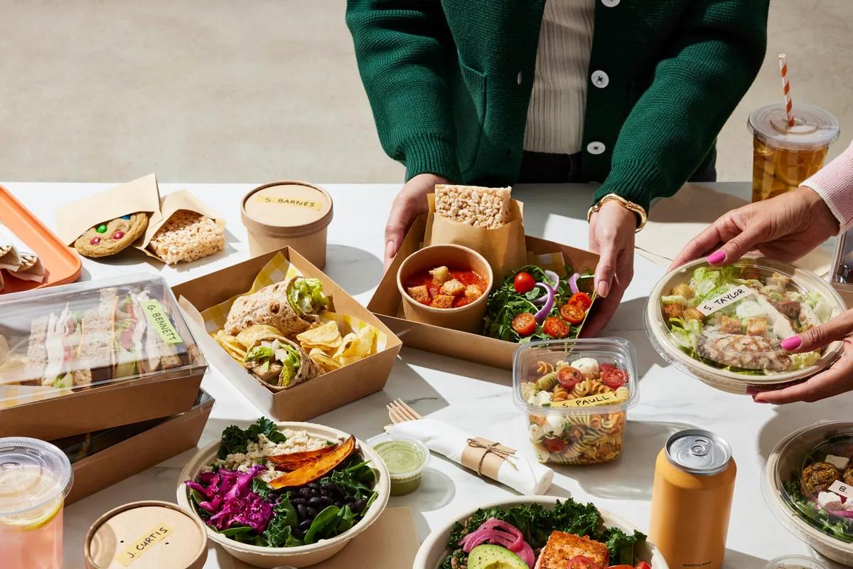 Colleagues' hands sharing boxed lunches and sandwiches at a table, seen from above