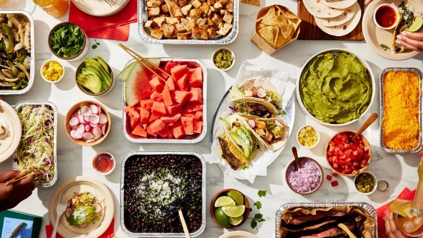 A build-your-own taco table with guacamole, black beans, steak and fruit