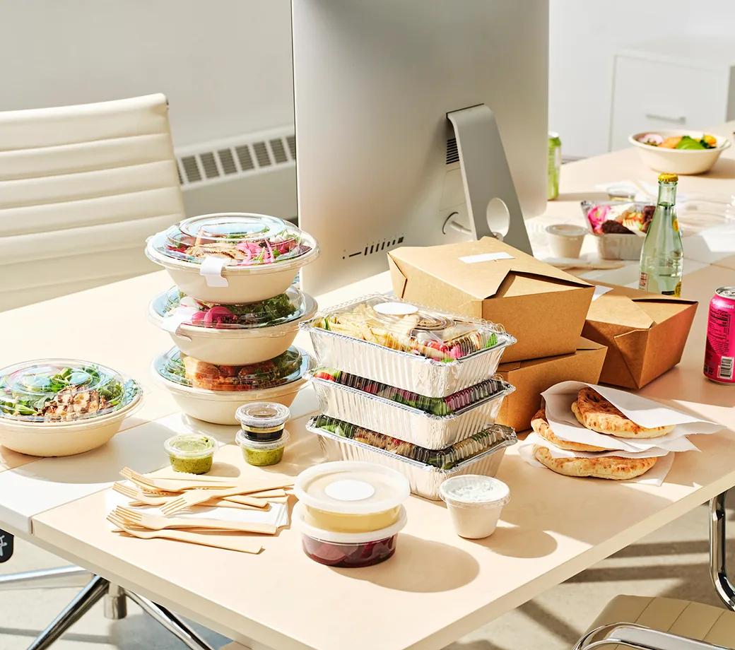 Packed lunches stacked on an office desk beside a monitor