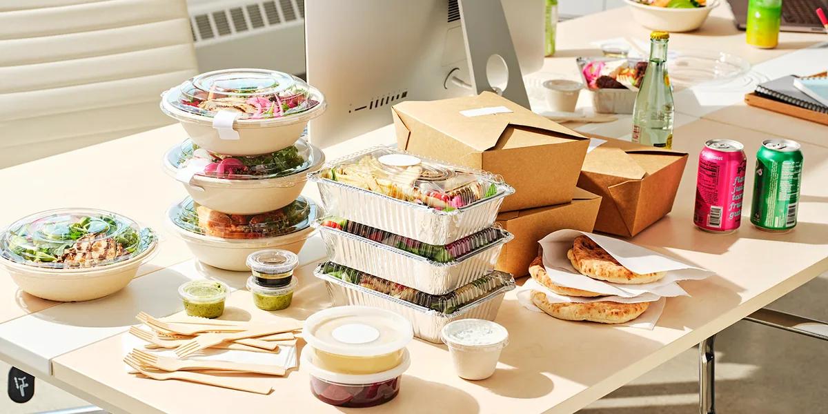 Packed lunches stacked on an office desk beside a monitor