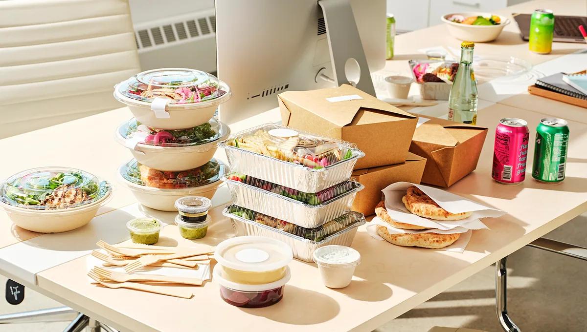 Packed lunches stacked on an office desk beside a monitor