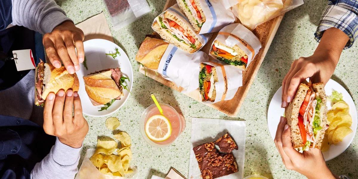 Colleagues holding wrapped sandwiches at a shared lunch table