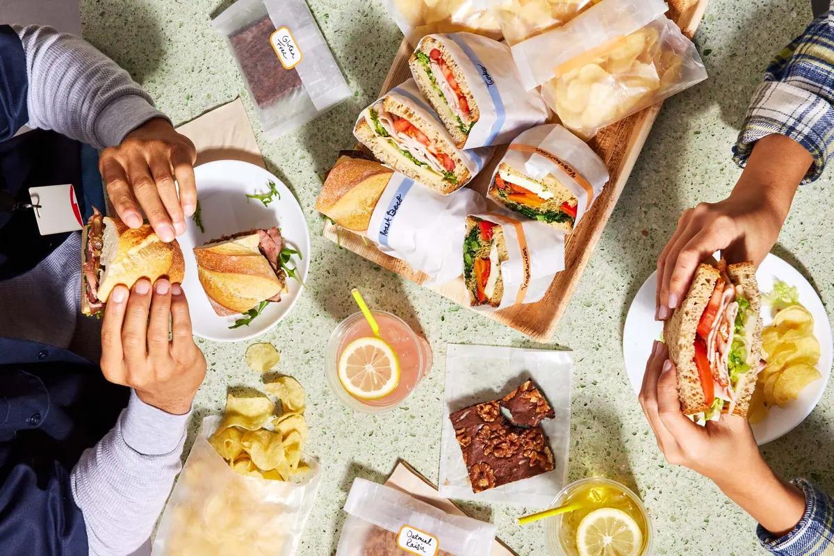 Colleagues holding wrapped sandwiches at a shared lunch table
